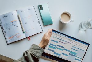 person holding ipad near white ceramic mug and laptop